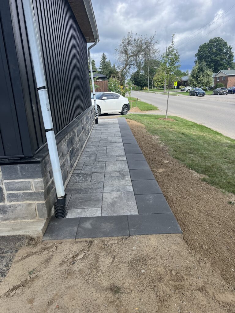 Interlocking paver side walkway with dark border beside home, graded away from the foundation, North Bay, Ontario